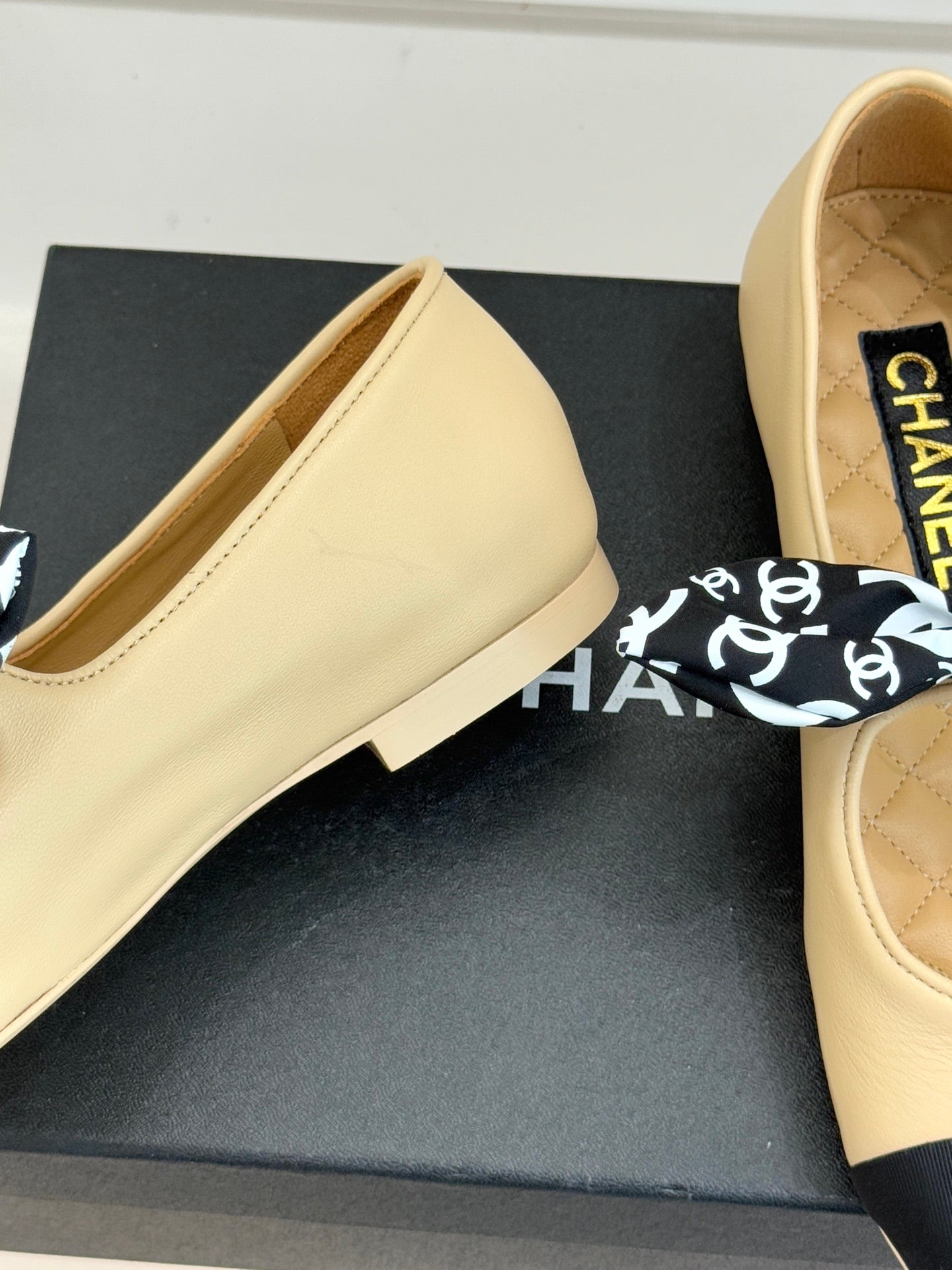 Beige flats close-up with navy sole edge; black logo bow detail on upper
