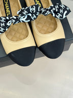 Pair of beige flats with navy toe caps and black CHANEL logo bow; quilted footbeds