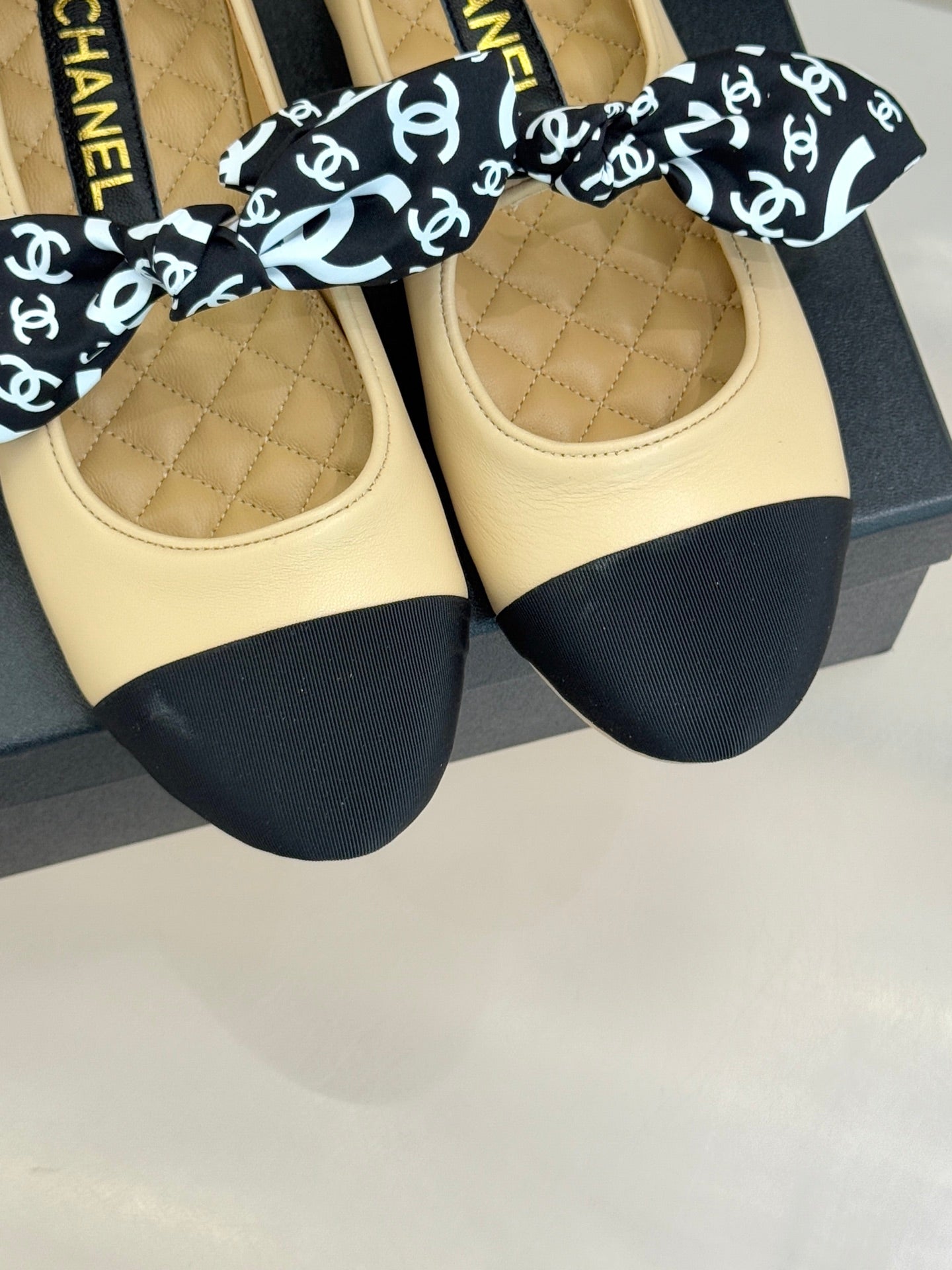 Pair of beige flats with navy toe caps and black CHANEL logo bow; quilted footbeds