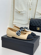 Beige flats with dark navy toe and black patterned bow, leather upper and rounded tip