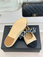 Beige flat with navy toe cap and black logo bow; outsole view on display box