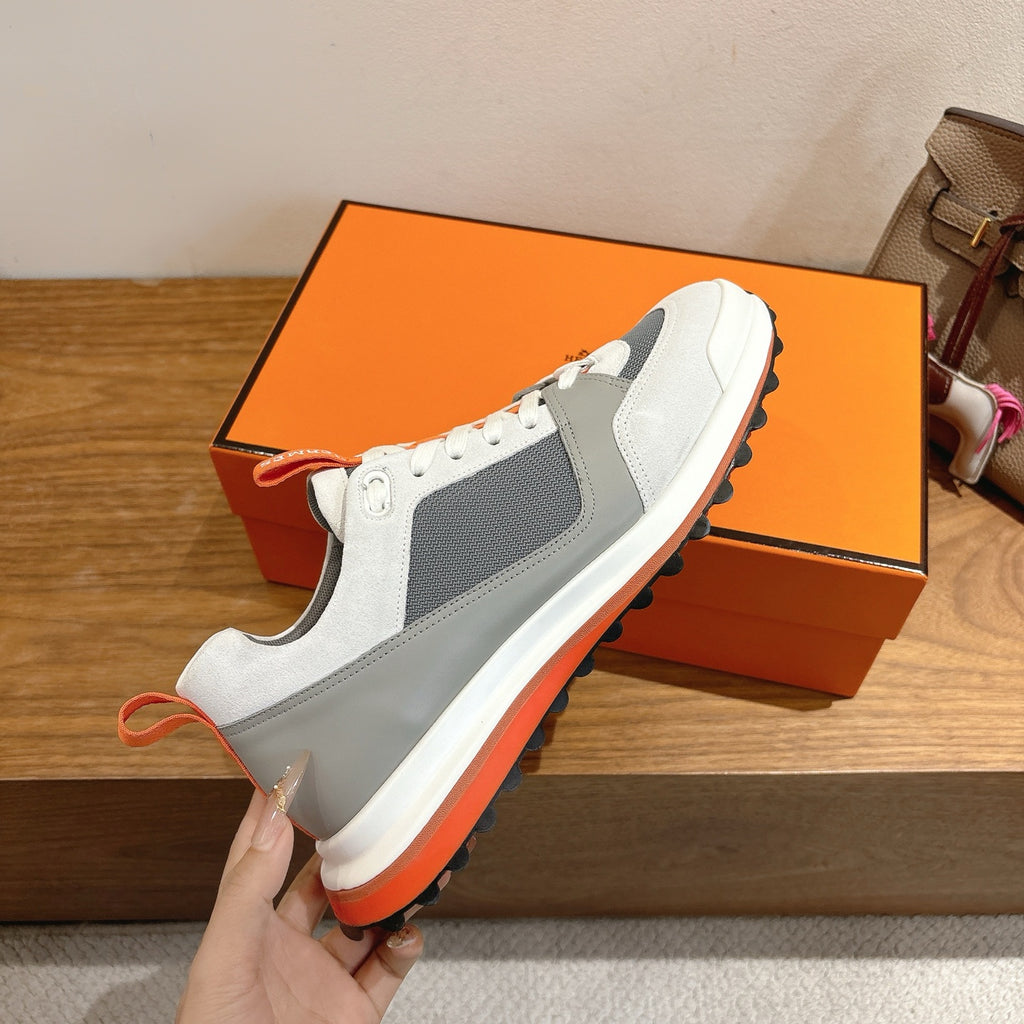 Hermes unisex sneaker held up, white with gray paneling and orange outsole