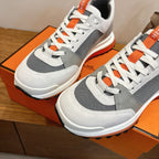 Hermes unisex sneakers close-up, white upper with gray overlays and orange laces