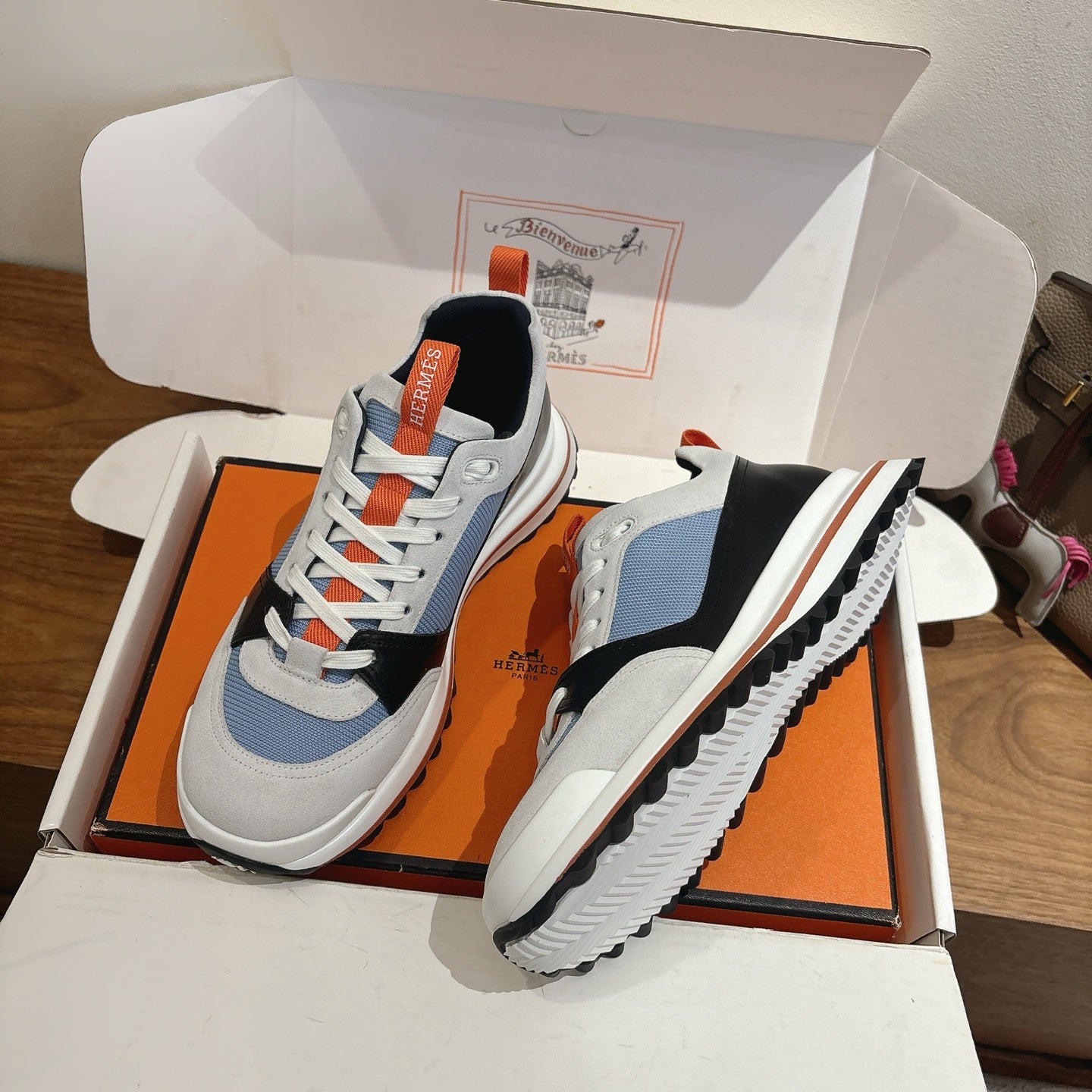 Unisex sneakers in open box: white and light blue upper with black side and orange laces