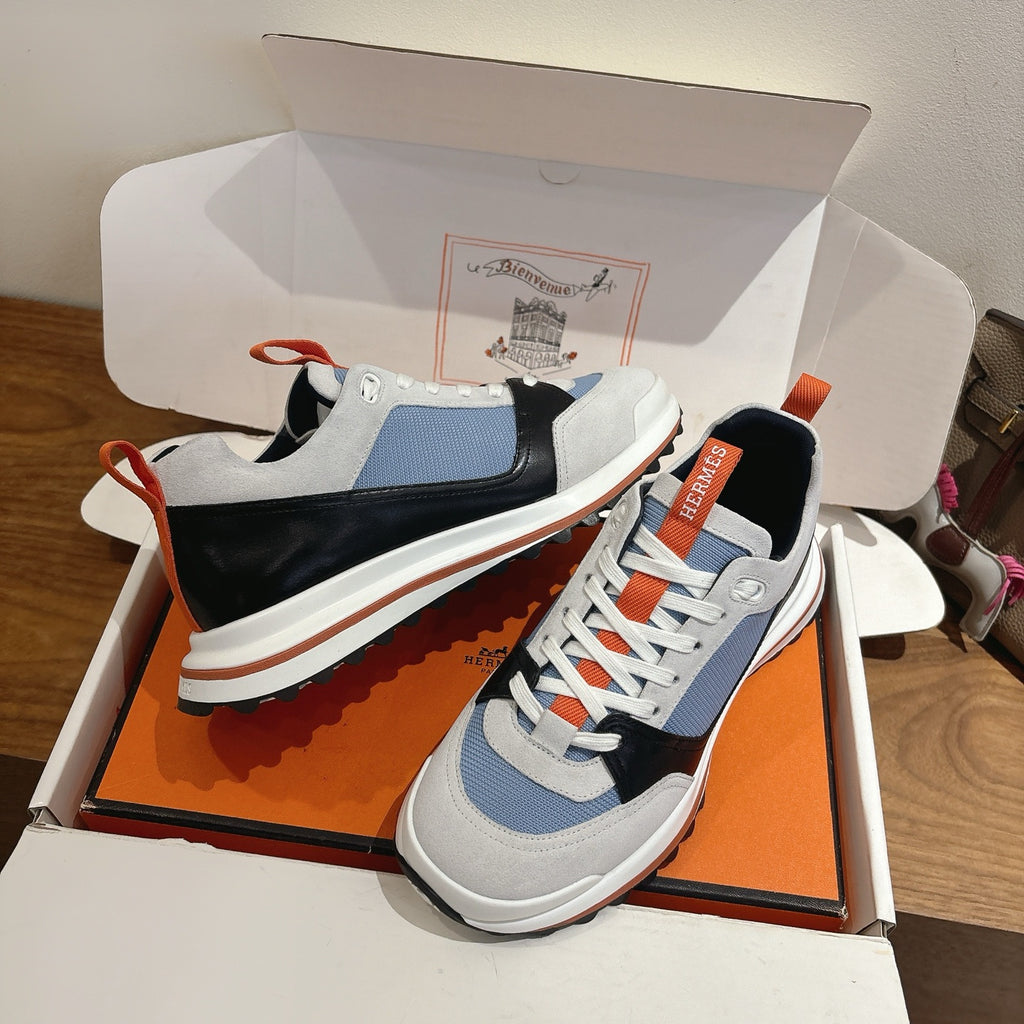 Unisex sneakers in open shoebox; white soles, light blue panels, black toe, orange lace trim