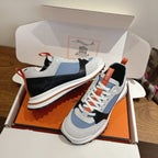 Unisex sneakers in open shoebox; white soles, light blue panels, black toe, orange lace trim
