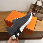 Unisex sneakers, dark upper with white laces and ridged white sole on orange box