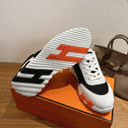 White and black sneakers with orange tread accents and ribbed outsole