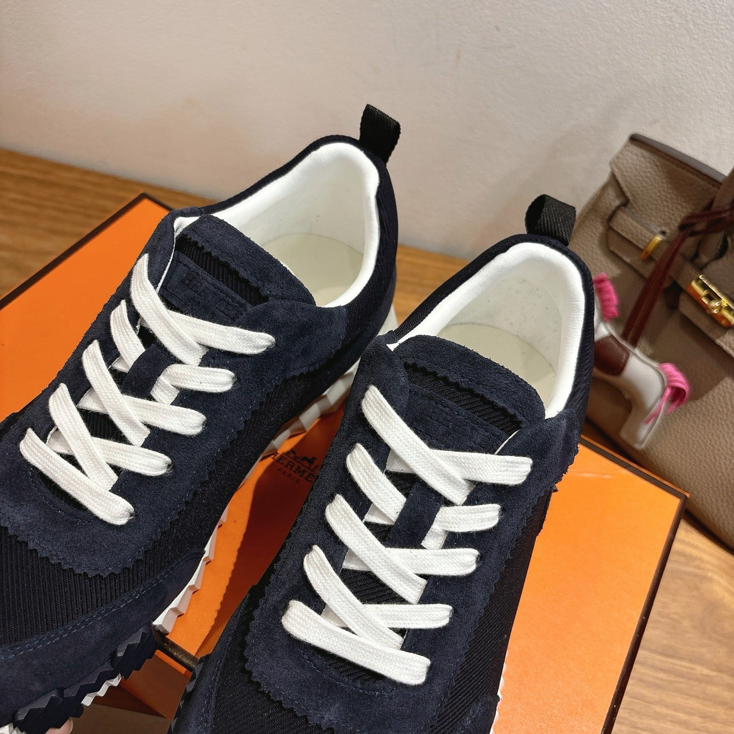 Unisex Hermes sneaker close-up, dark navy suede with white lace-up and stitched trim