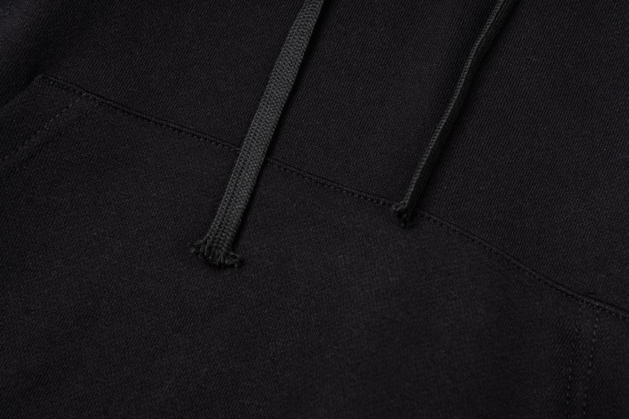 Black hoodie close-up showing kangaroo pocket opening and stitched hem