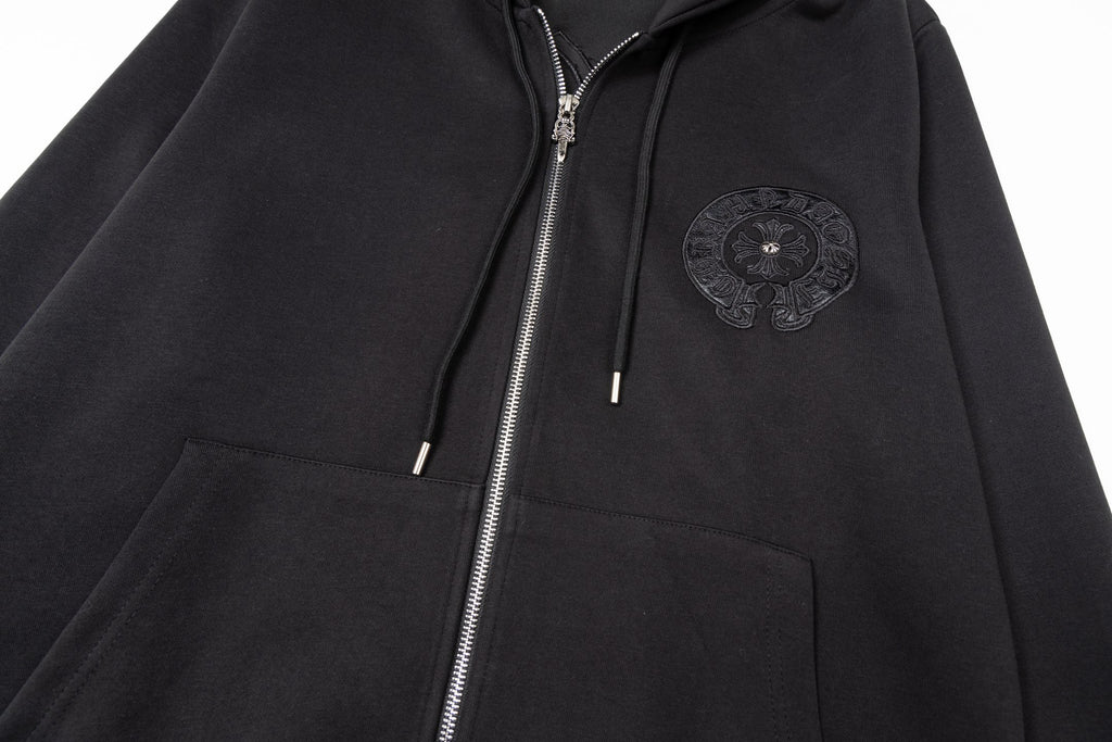 Black zip-up hoodie close-up with embroidered chest emblem, hood, and drawstrings