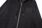 Black zip-up hoodie close-up with embroidered chest emblem, hood, and drawstrings