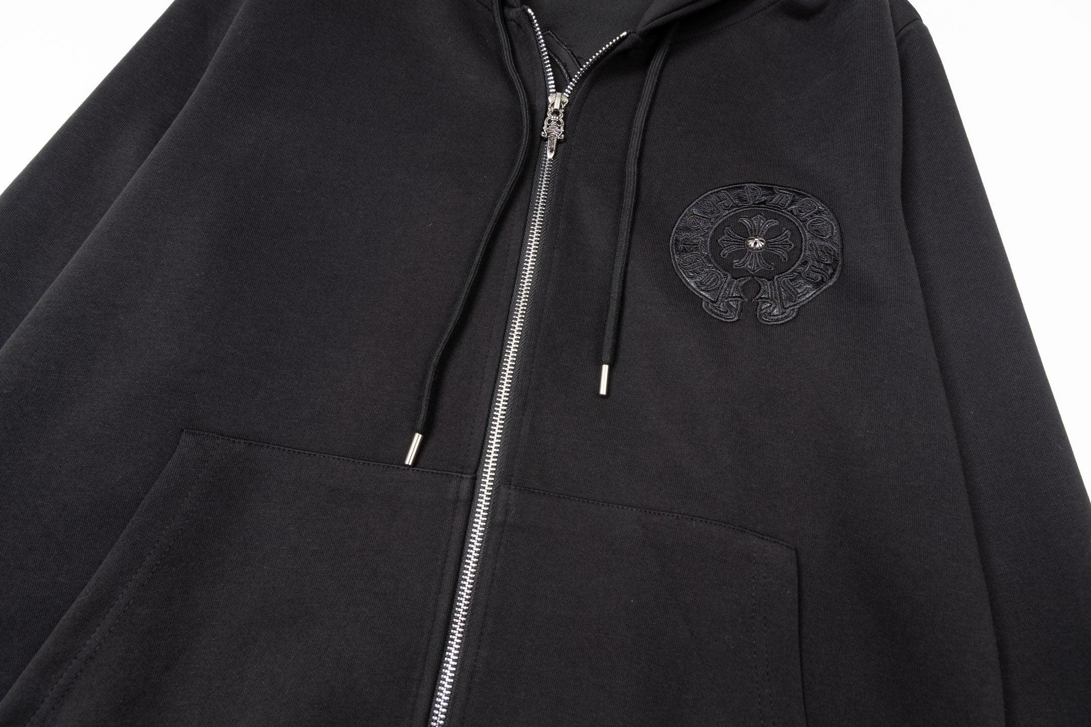 Black zip-up hoodie close-up with embroidered chest emblem, hood, and drawstrings