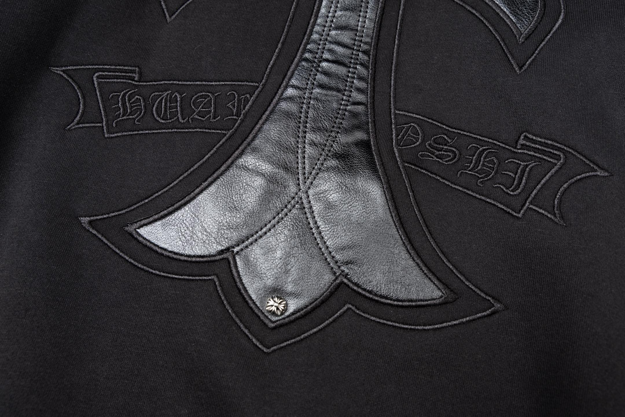 Black zip-up jacket front with chrome-style cross applique and stitched seams