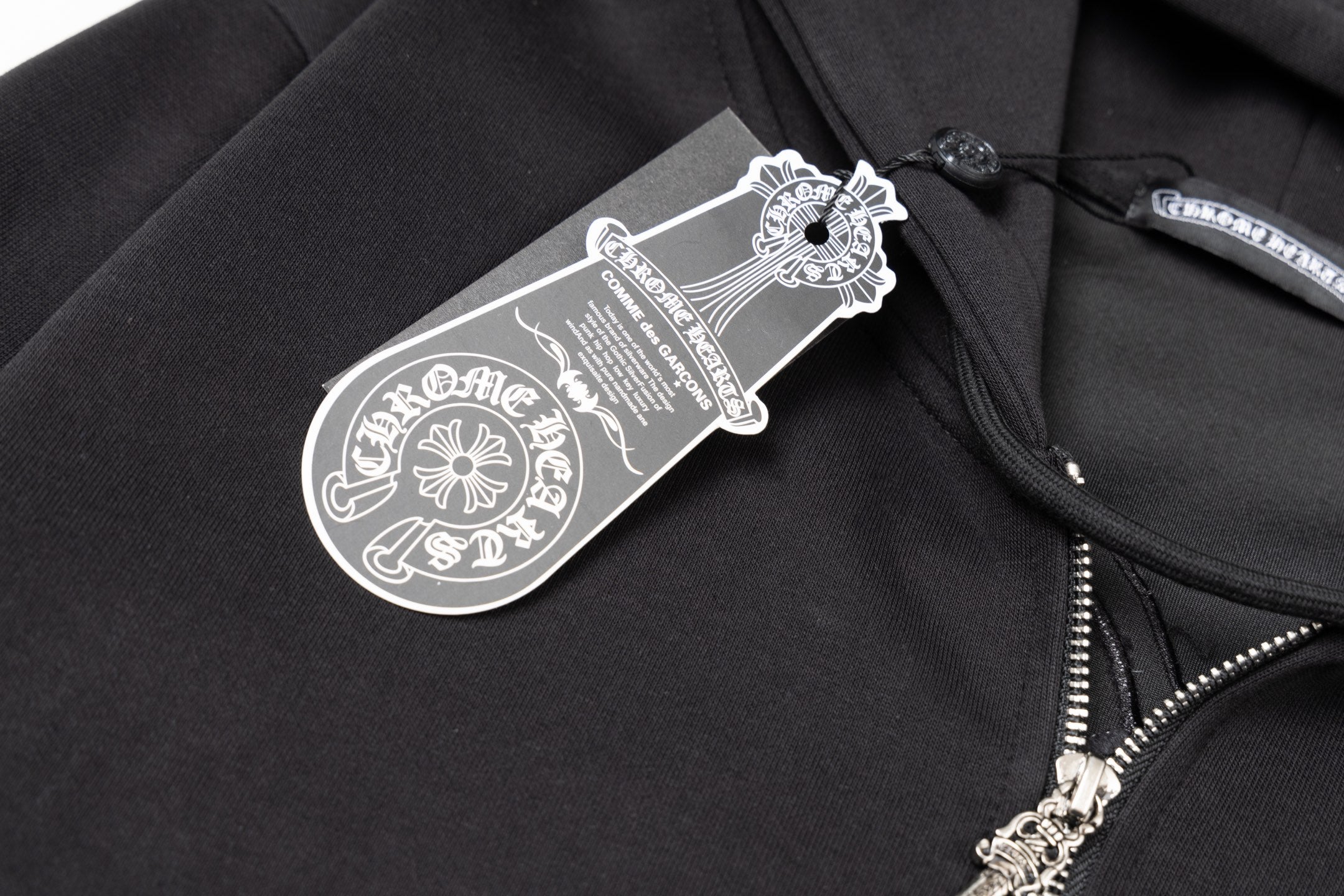 Black hoodie close-up with hanging brand tag near the zipper and pocket