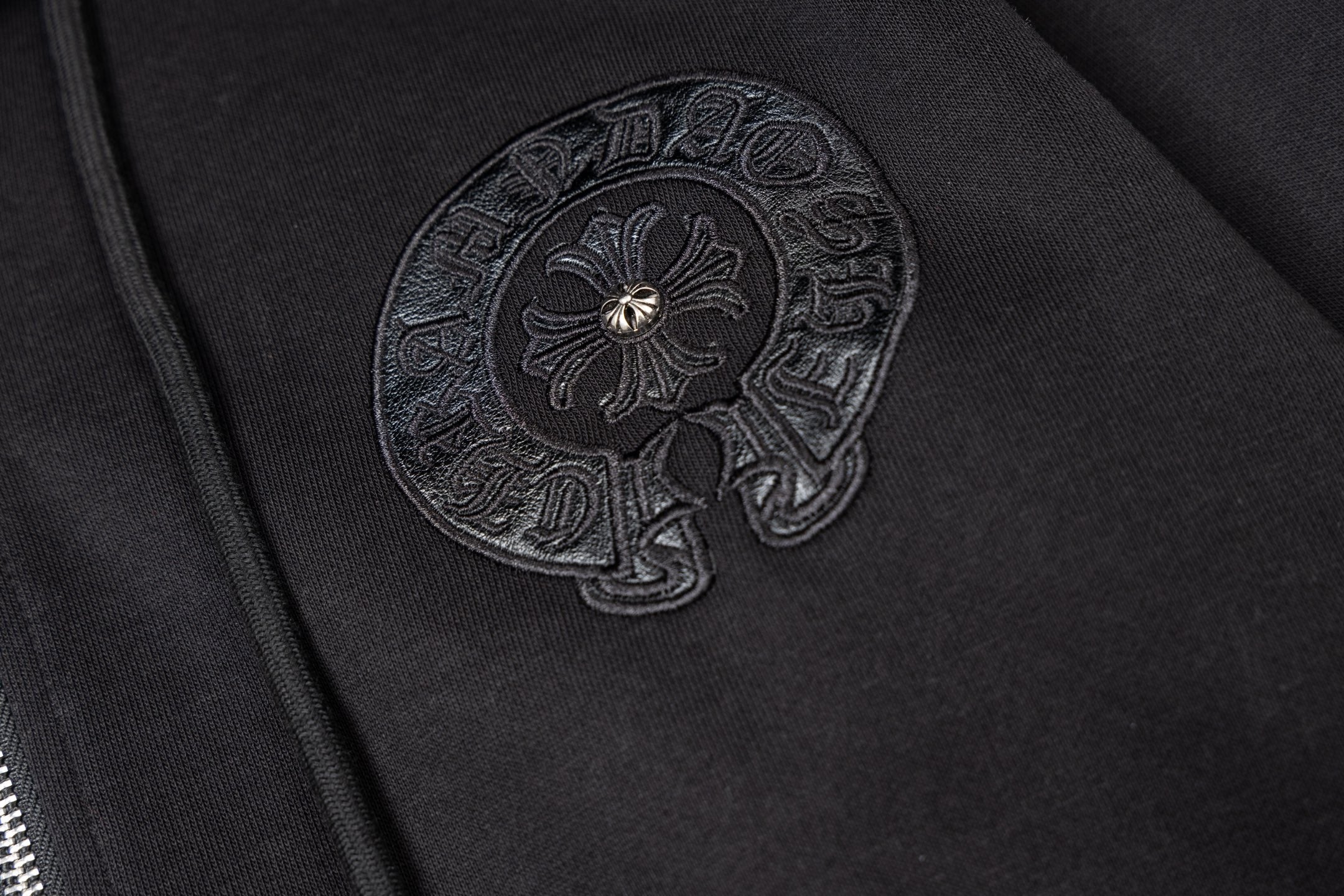 Black hoodie side close-up with embroidered round emblem patch