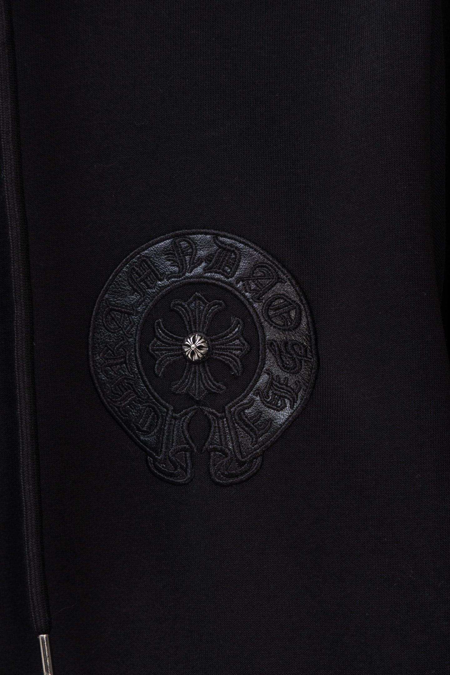 Black zip-up hoodie chest close-up with circular embossed emblem