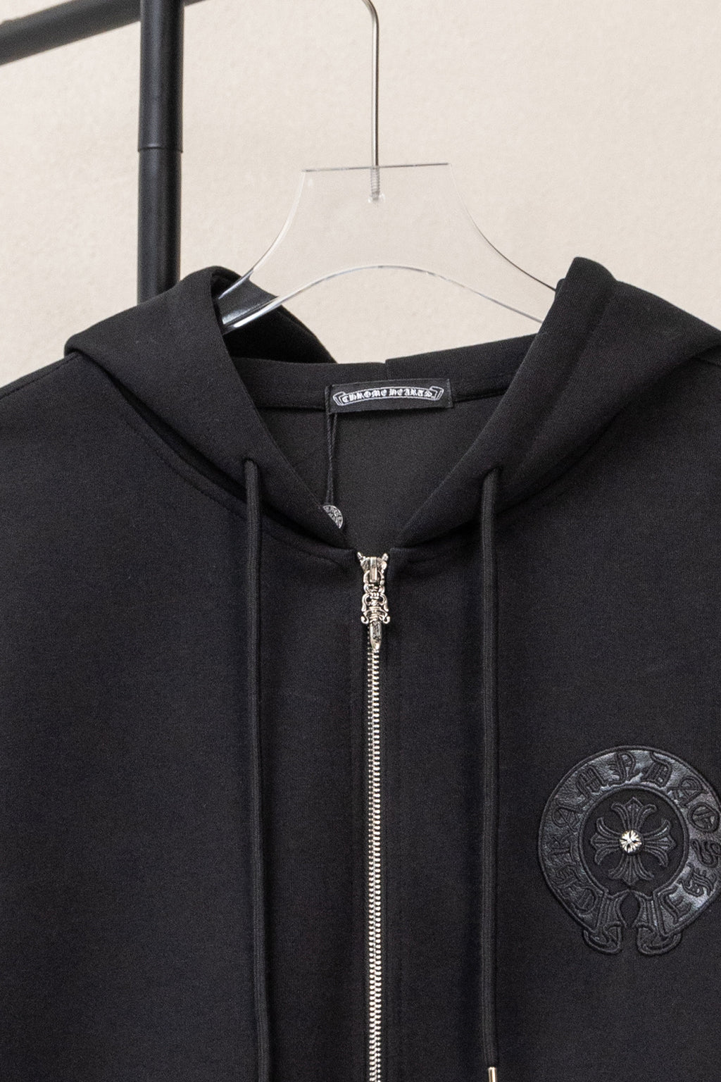 Black zip-up hoodie close-up at hood with metal zipper and circular chest emblem