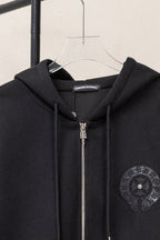 Black zip-up hoodie close-up at hood with metal zipper and circular chest emblem