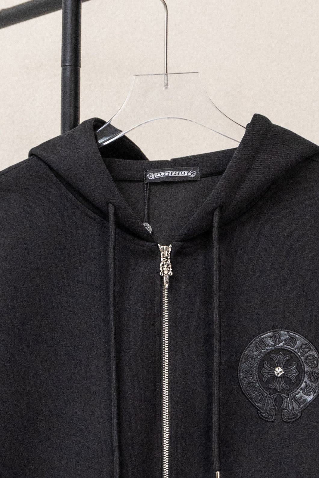 Black zip-up hoodie close-up at hood with metal zipper and circular chest emblem