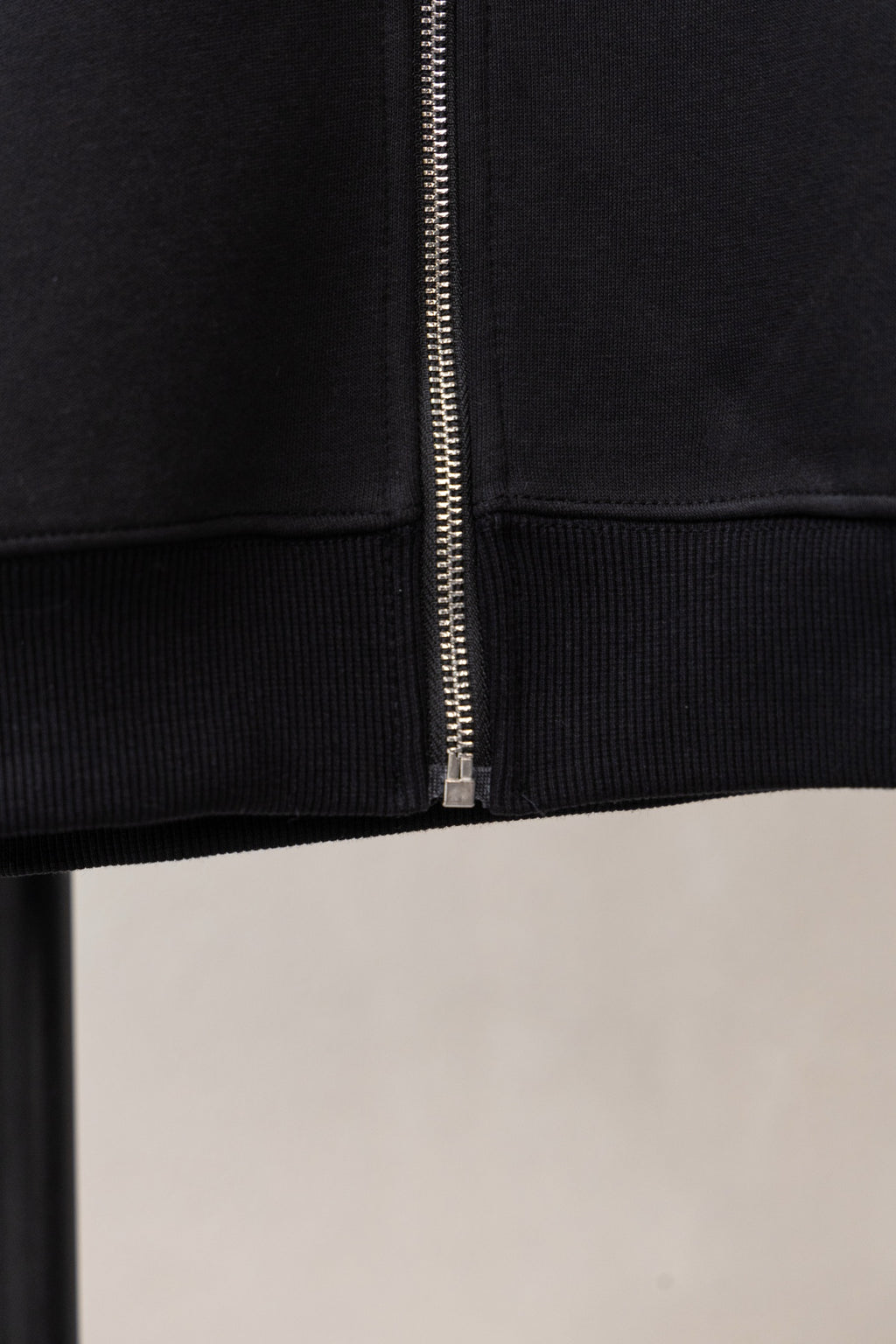Black zip hoodie close-up: center zipper and ribbed cuffs