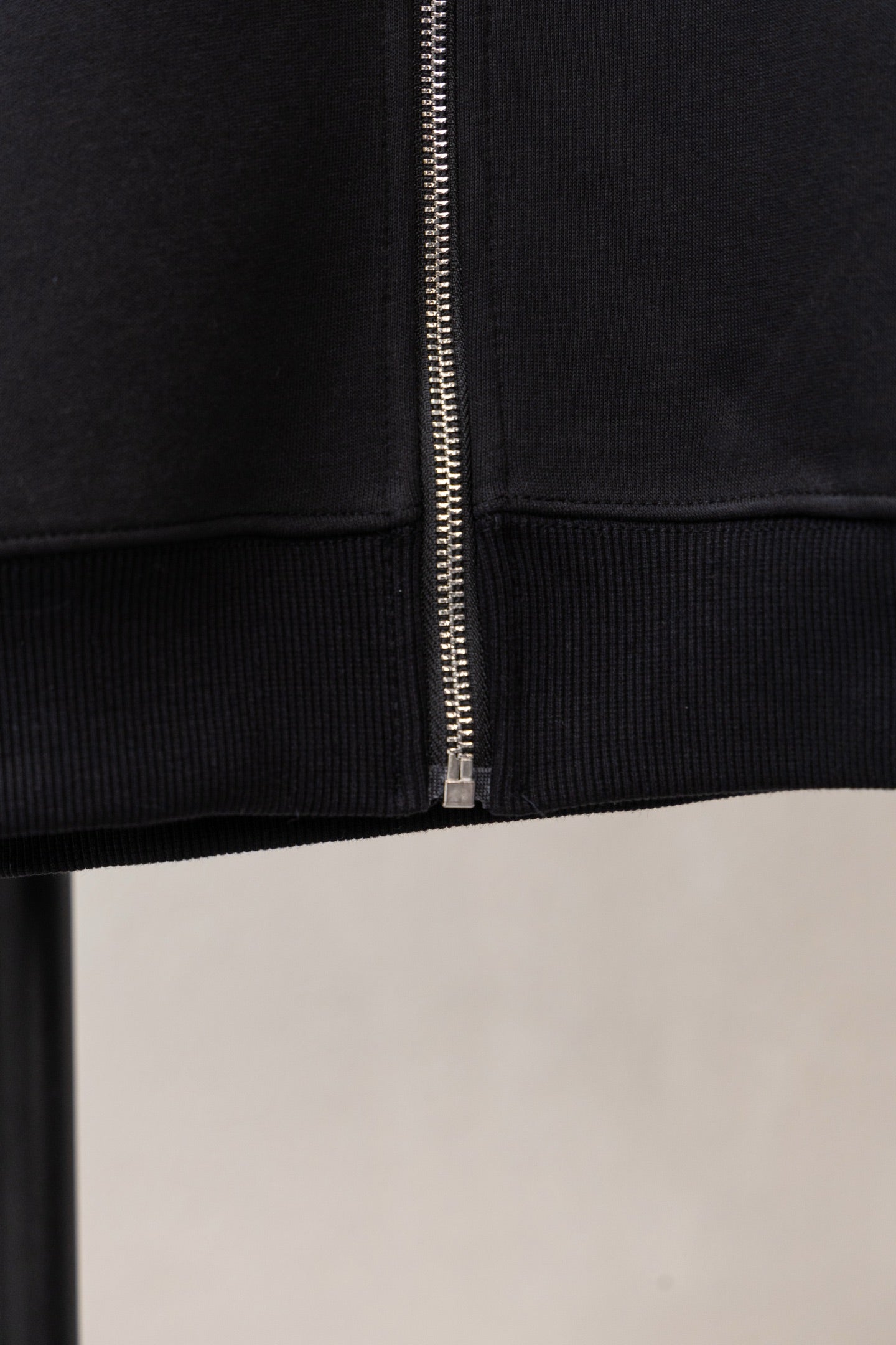 Black zip hoodie close-up: center zipper and ribbed cuffs