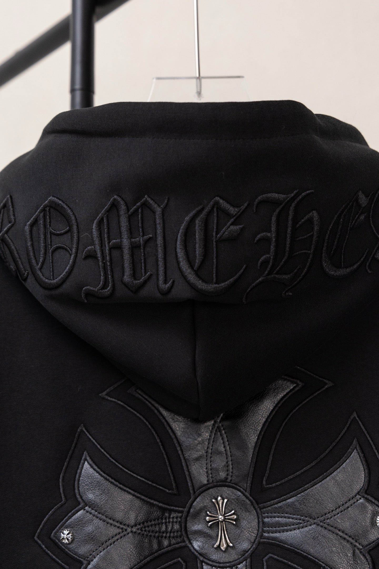 Black zip-up hoodie back close-up with large floral cross graphic and embossed text