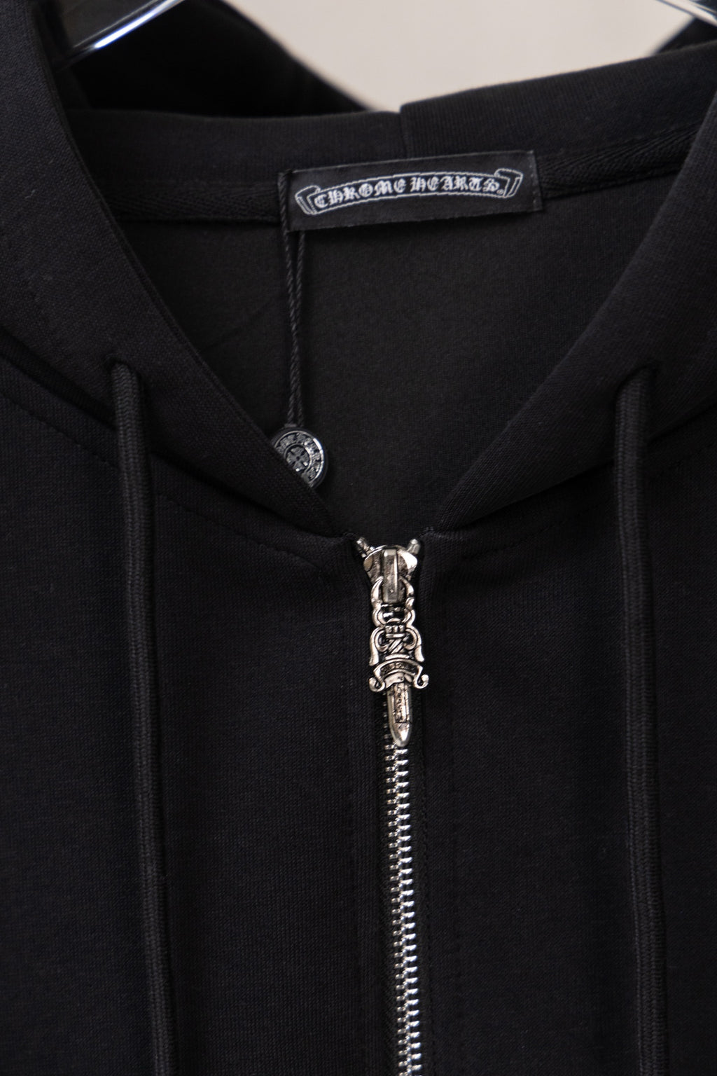 Black zip-up hoodie neckline close-up with hood tag and metal zipper pull