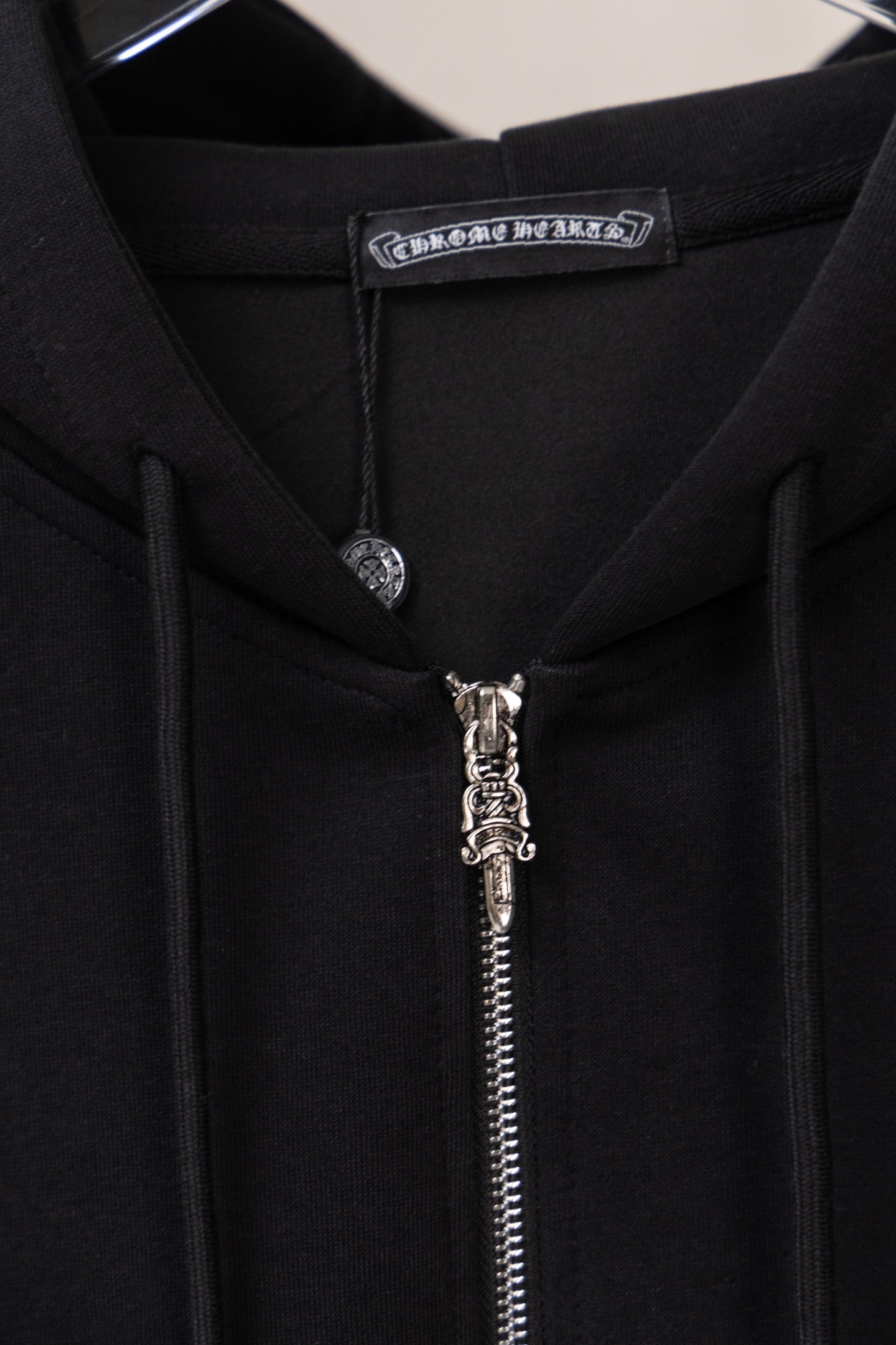 Black zip-up hoodie neckline close-up with hood tag and metal zipper pull