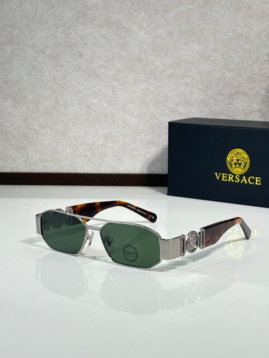 Sunglasses with silver frame and green gradient lenses, ornate logo detail on temple