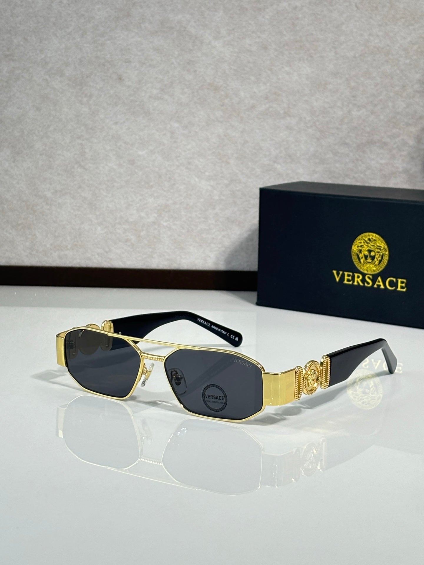Sunglasses with gold frame and dark lenses, ornate logo detail on temple