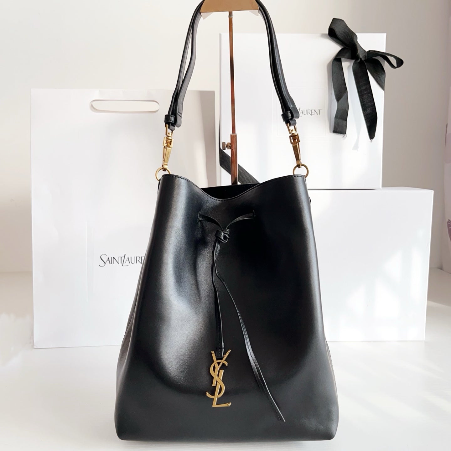 YSL black leather bucket bag with drawstring, gold YSL logo, and shoulder straps