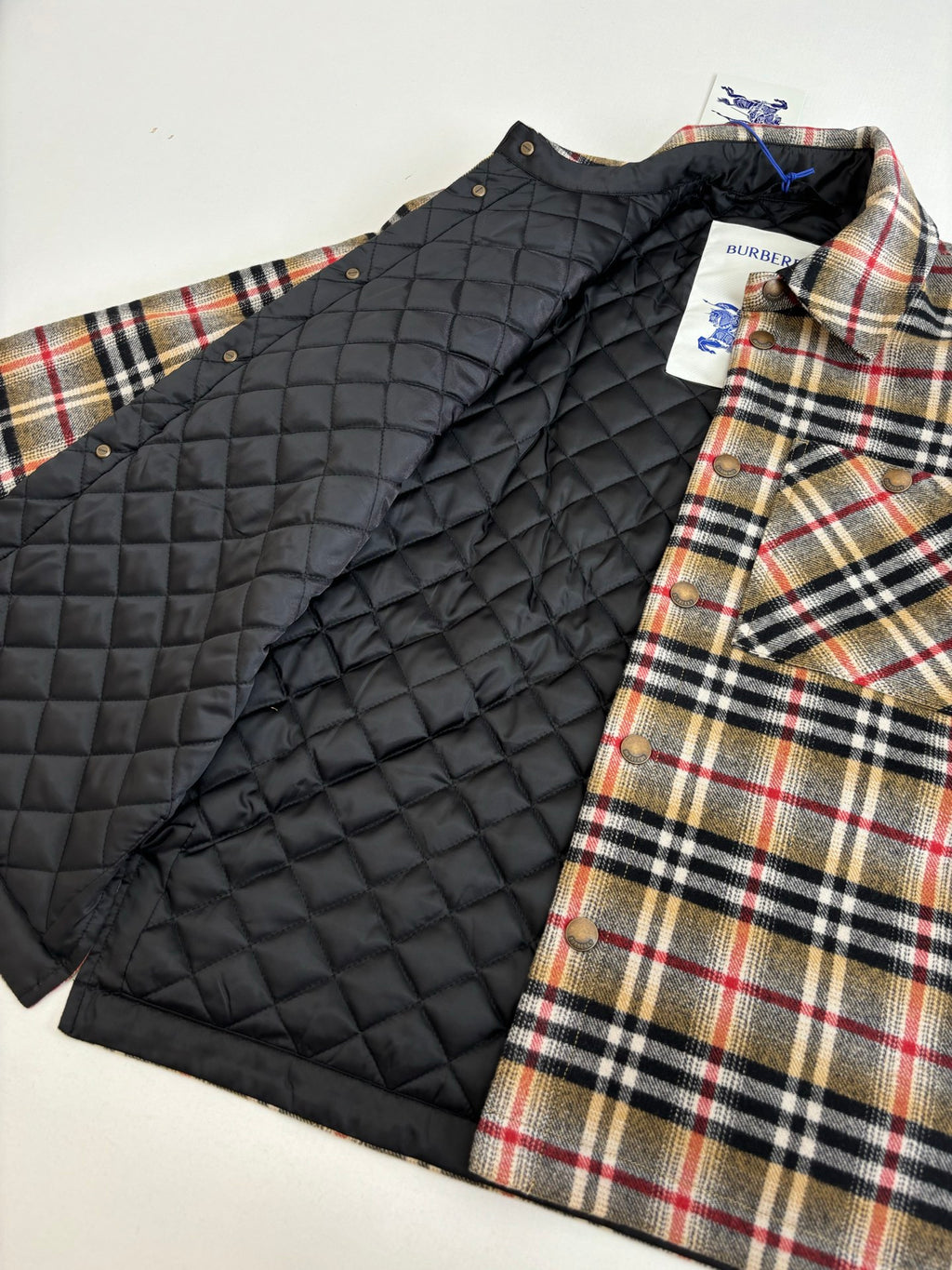 Burberry plaid outer shirt layered with black quilted puffer vest, close view
