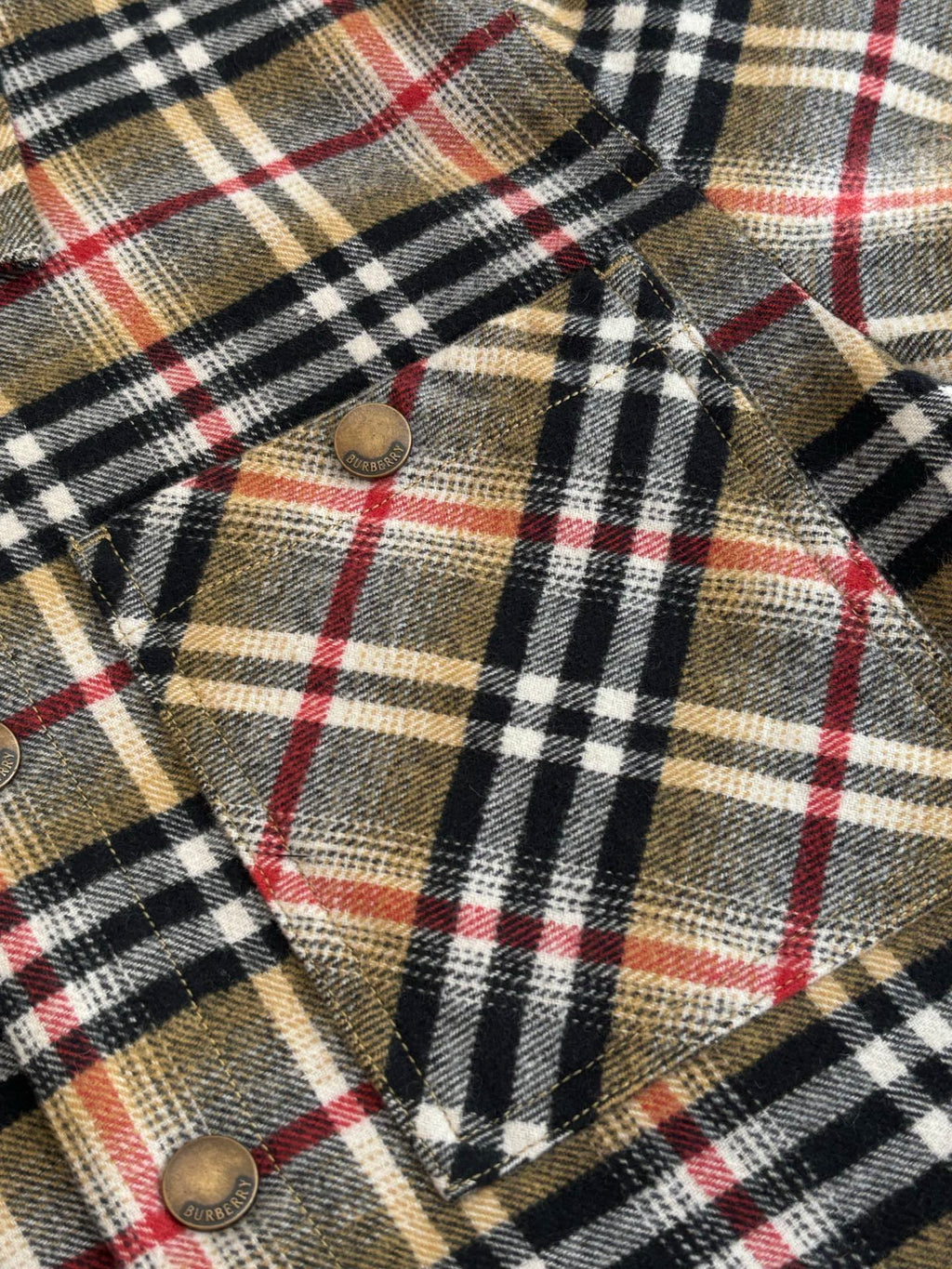 Burberry plaid fabric with metal buttons and pointed flap detail, close-up