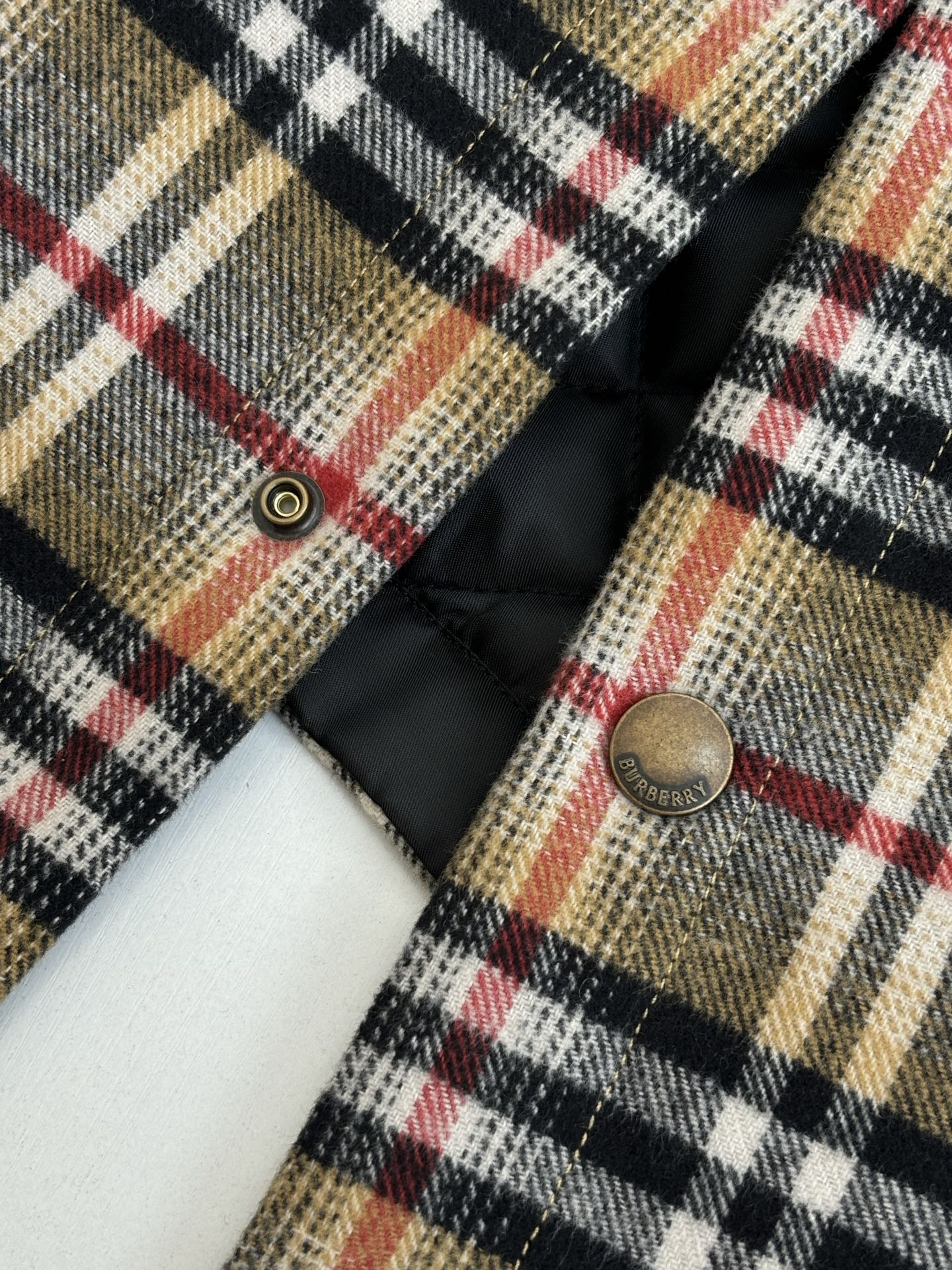 Plaid long-sleeve jacket front with metal snap buttons and black quilted lining