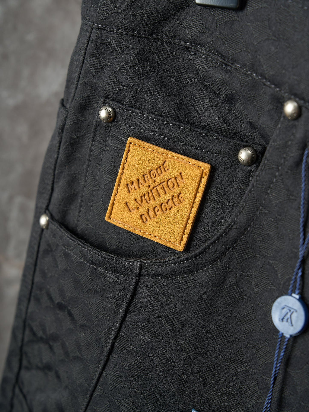 Louis Vuitton pants close-up of front pocket with tan logo patch and gold snap buttons