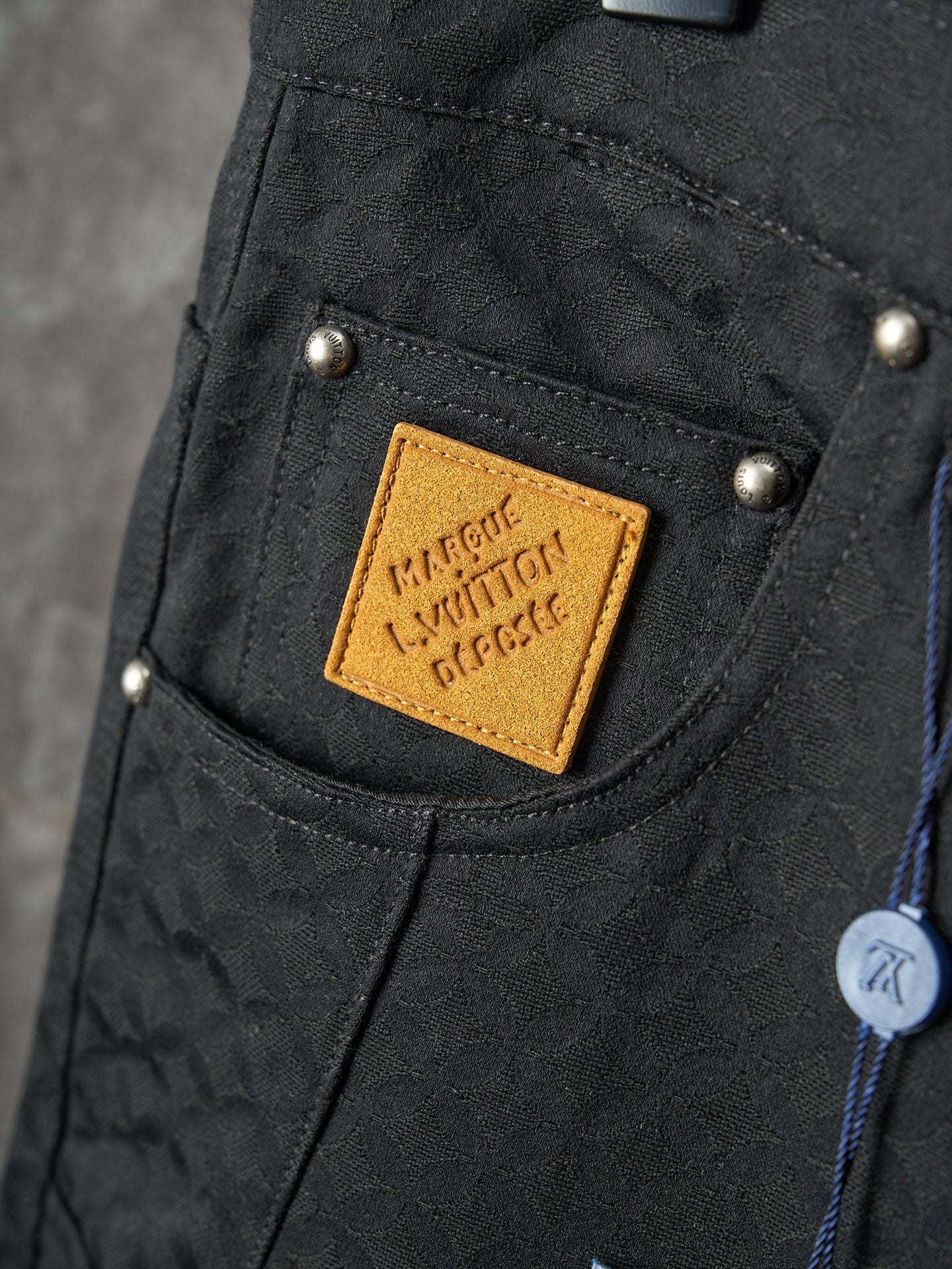Louis Vuitton pants close-up of front pocket with tan logo patch and gold snap buttons