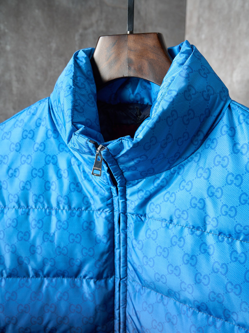 Blue hooded puffer jacket with monogram pattern, front zipper, and metal pull tab