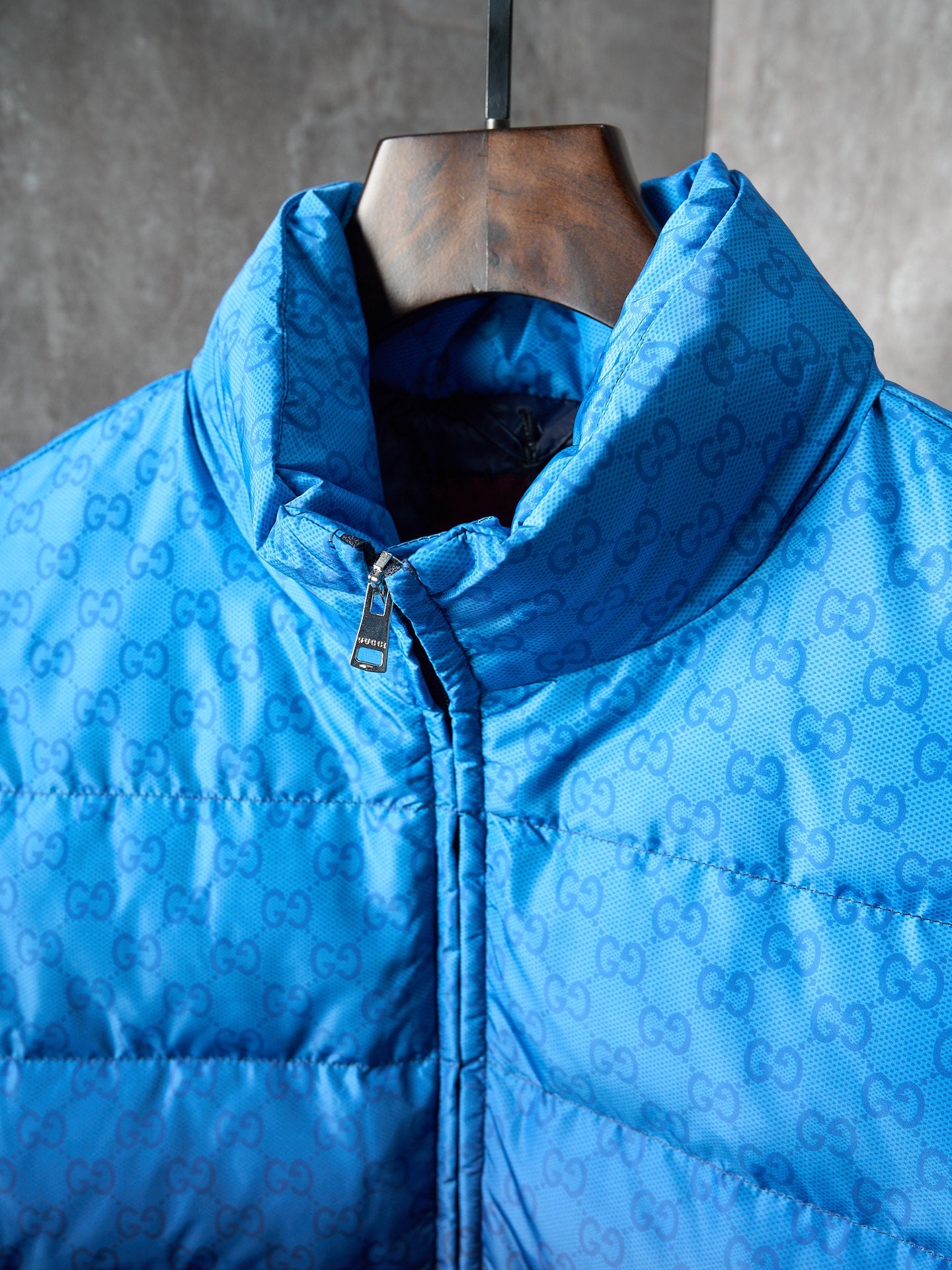 Blue hooded puffer jacket with monogram pattern, front zipper, and metal pull tab