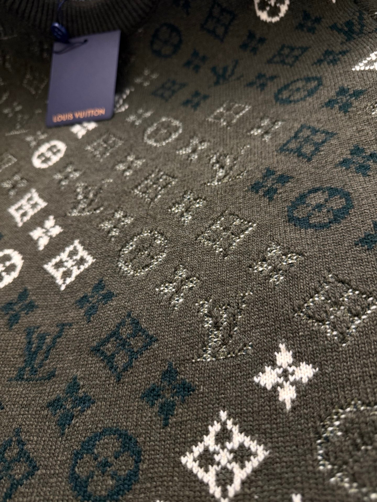 Brown knit sweater fabric detail with blue monogram icons and white motifs