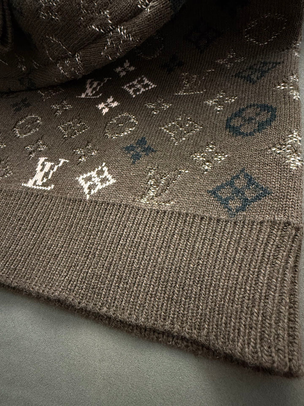 Brown knit sweater hem with ribbed cuff and small white monogram details