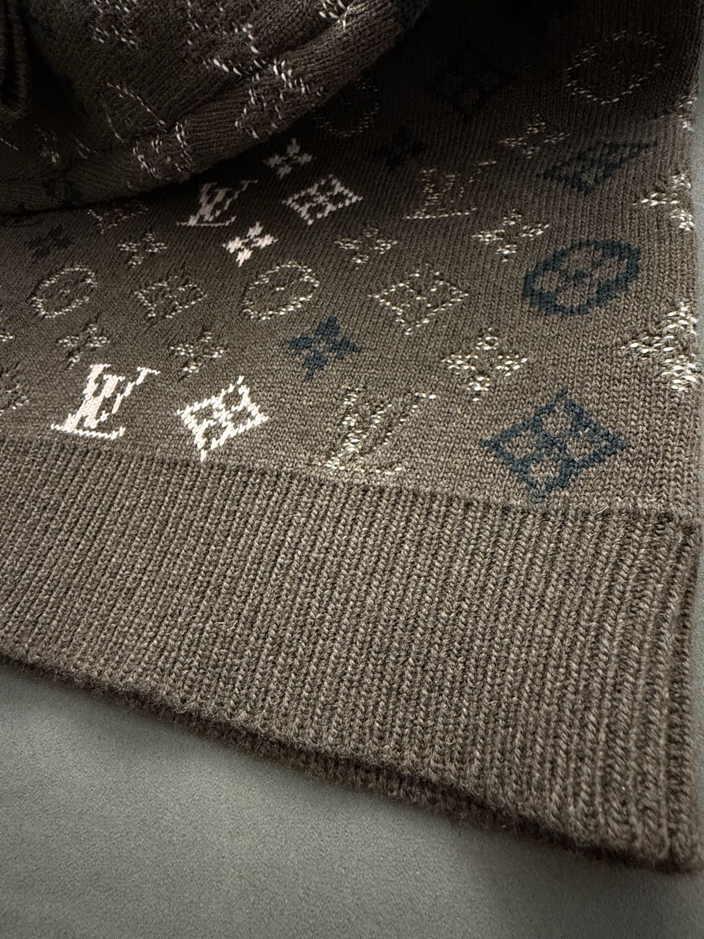 Brown knit sweater hem with ribbed cuff and small white monogram details