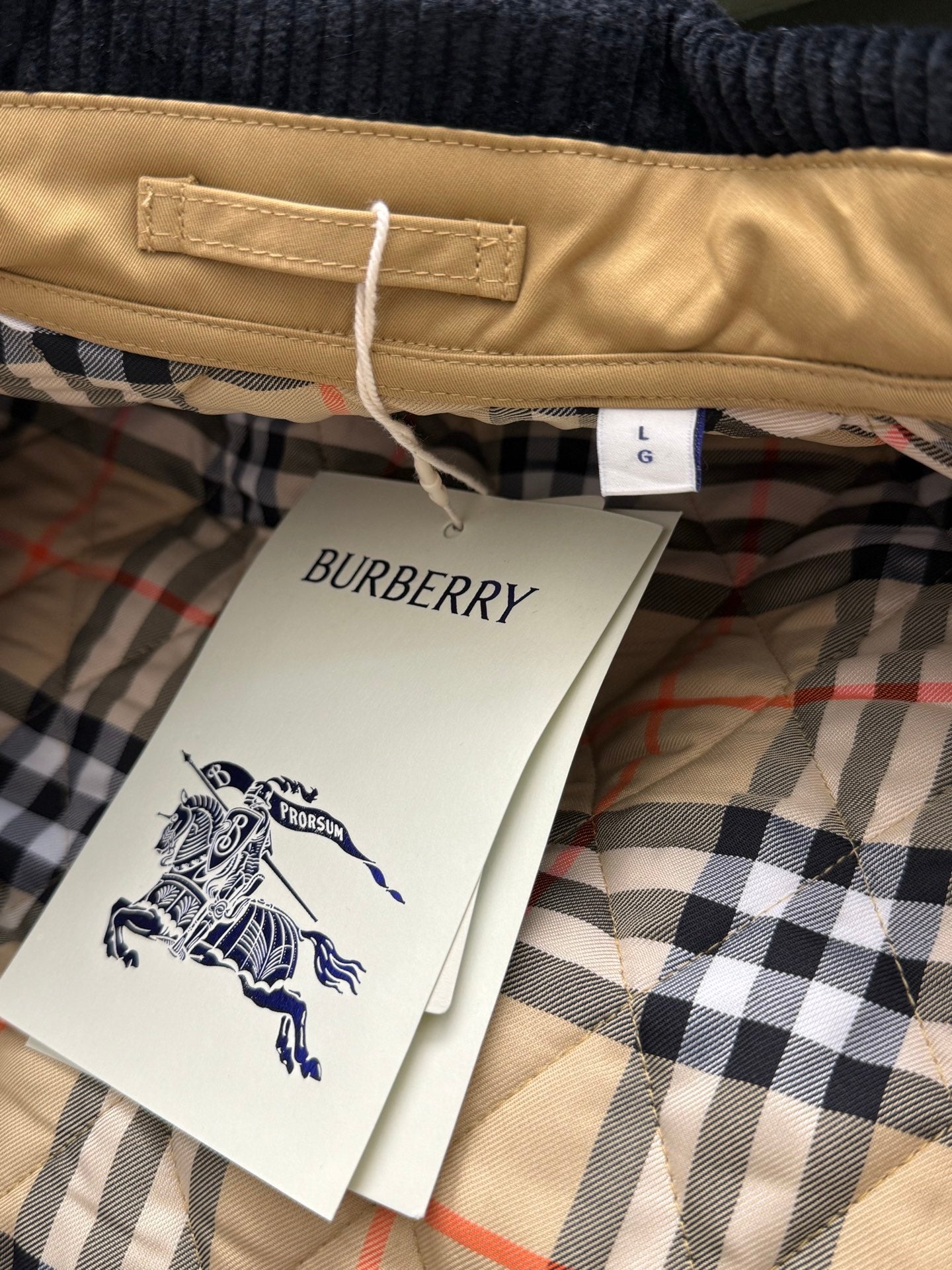Tan quilted jacket hem with size tag and Burberry product tag on plaid lining