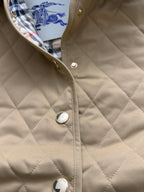 Quilted tan jacket front with snap buttons and round metal details