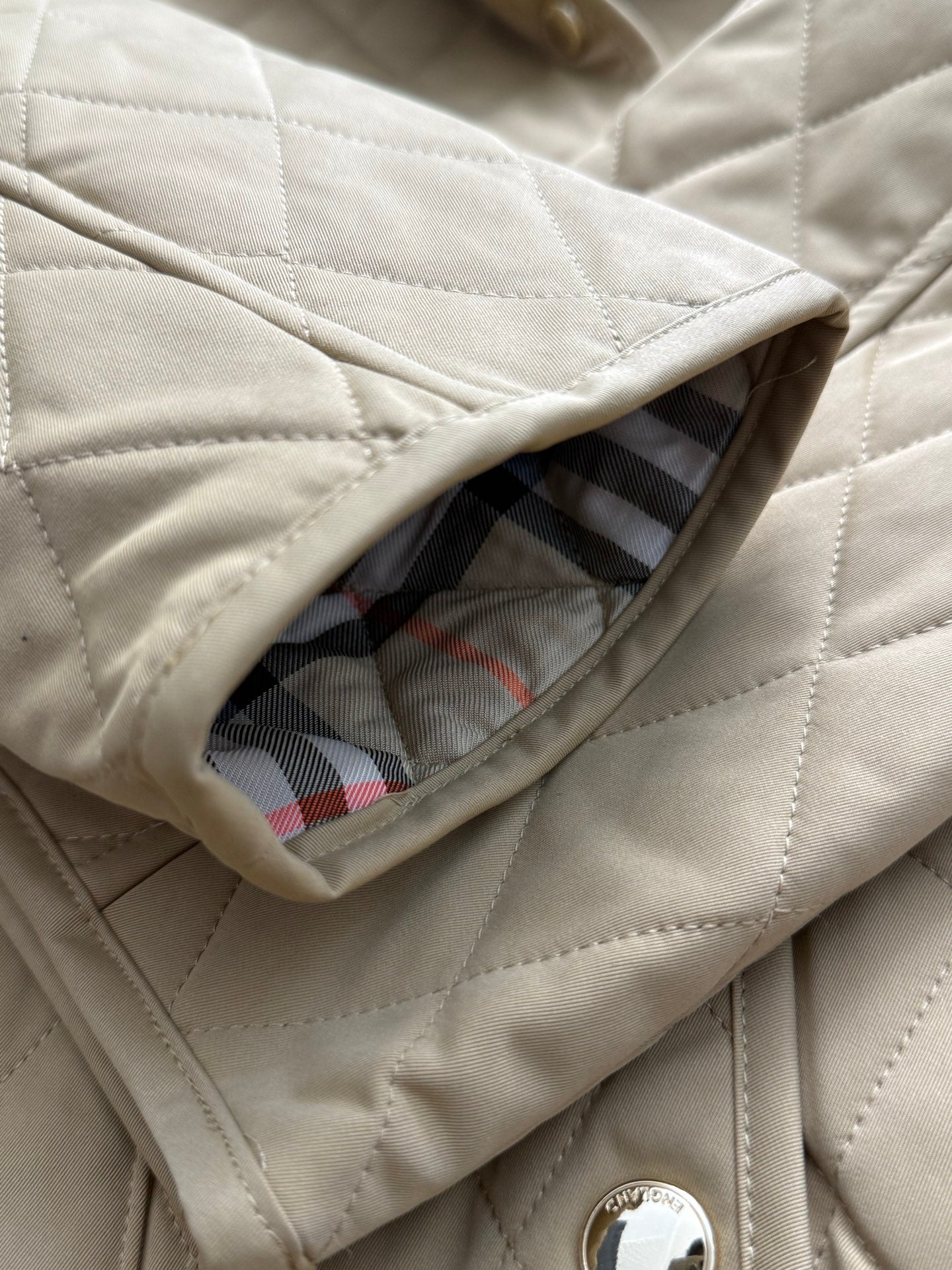 Tan quilted jacket sleeve cuff opening with plaid lining peeking through