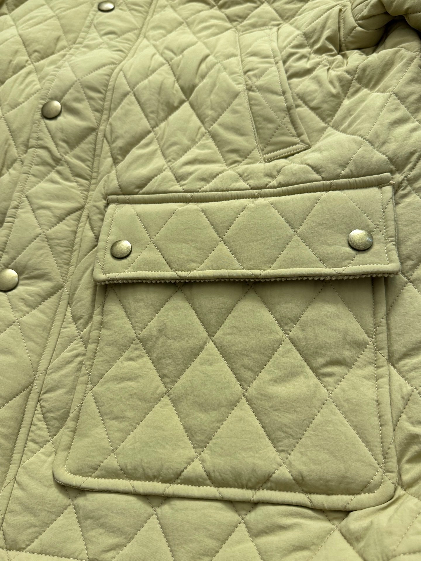 Light yellow quilted jacket front with flap patch pocket and snap buttons