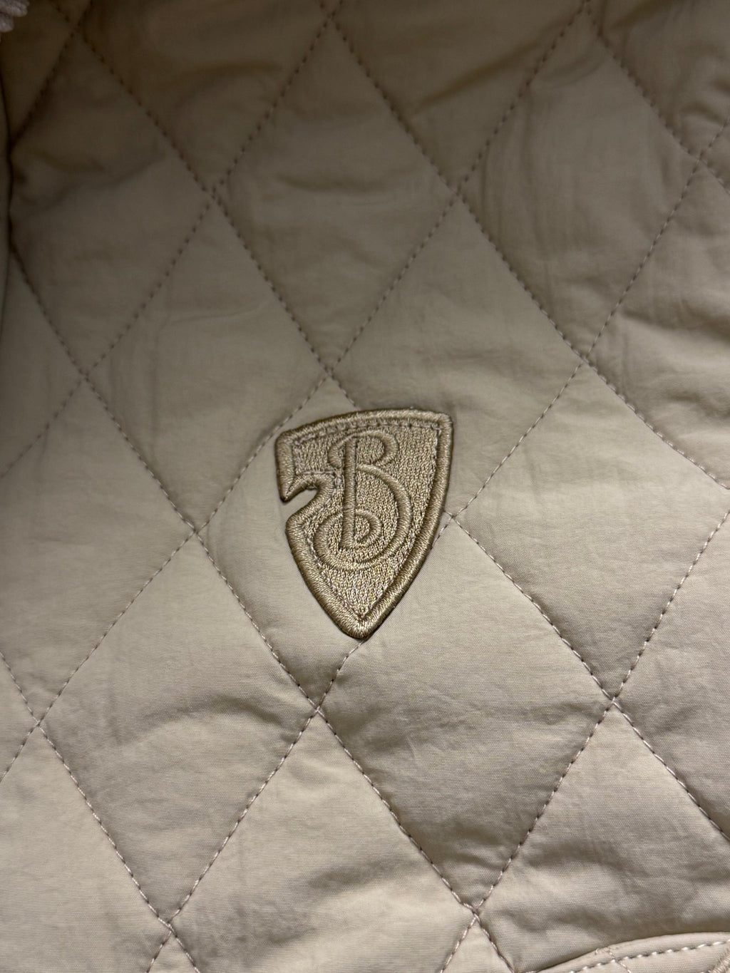 Embroidered shield logo patch on light yellow quilted jacket