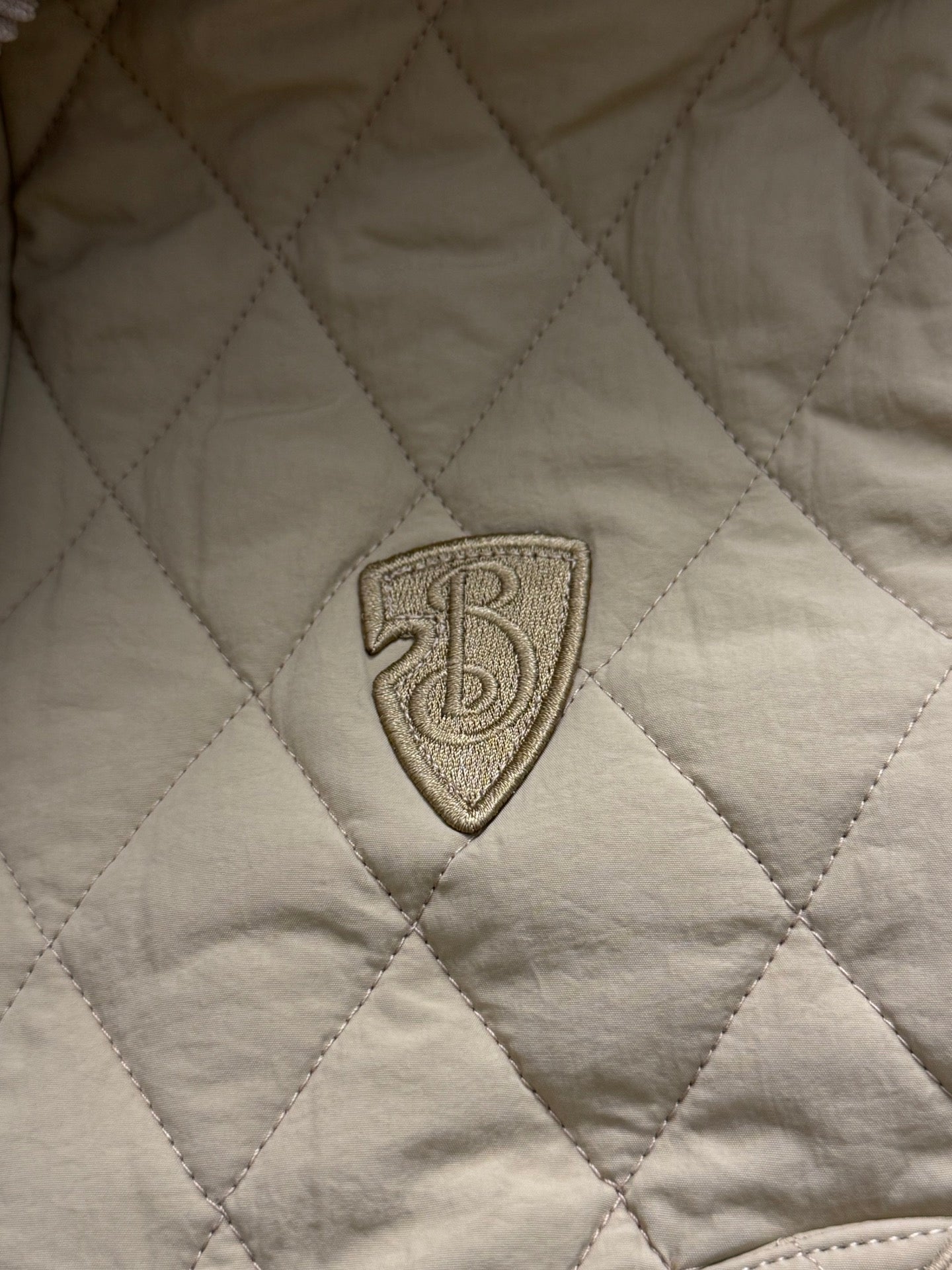 Embroidered shield logo patch on light yellow quilted jacket