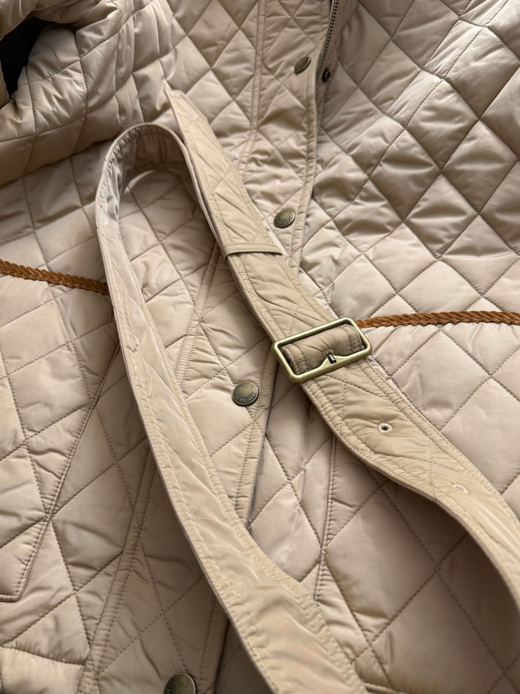 Quilted jacket shoulder with snap buttons, belted strap detail, and brass-toned hardware