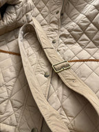 Quilted jacket shoulder with snap buttons, belted strap detail, and brass-toned hardware
